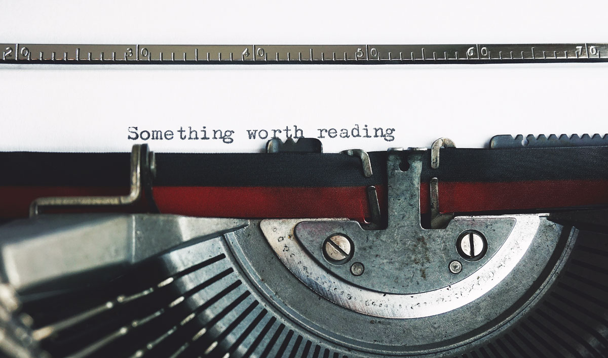 Red and black typewriter with the words "Something worth reading" typed on paper