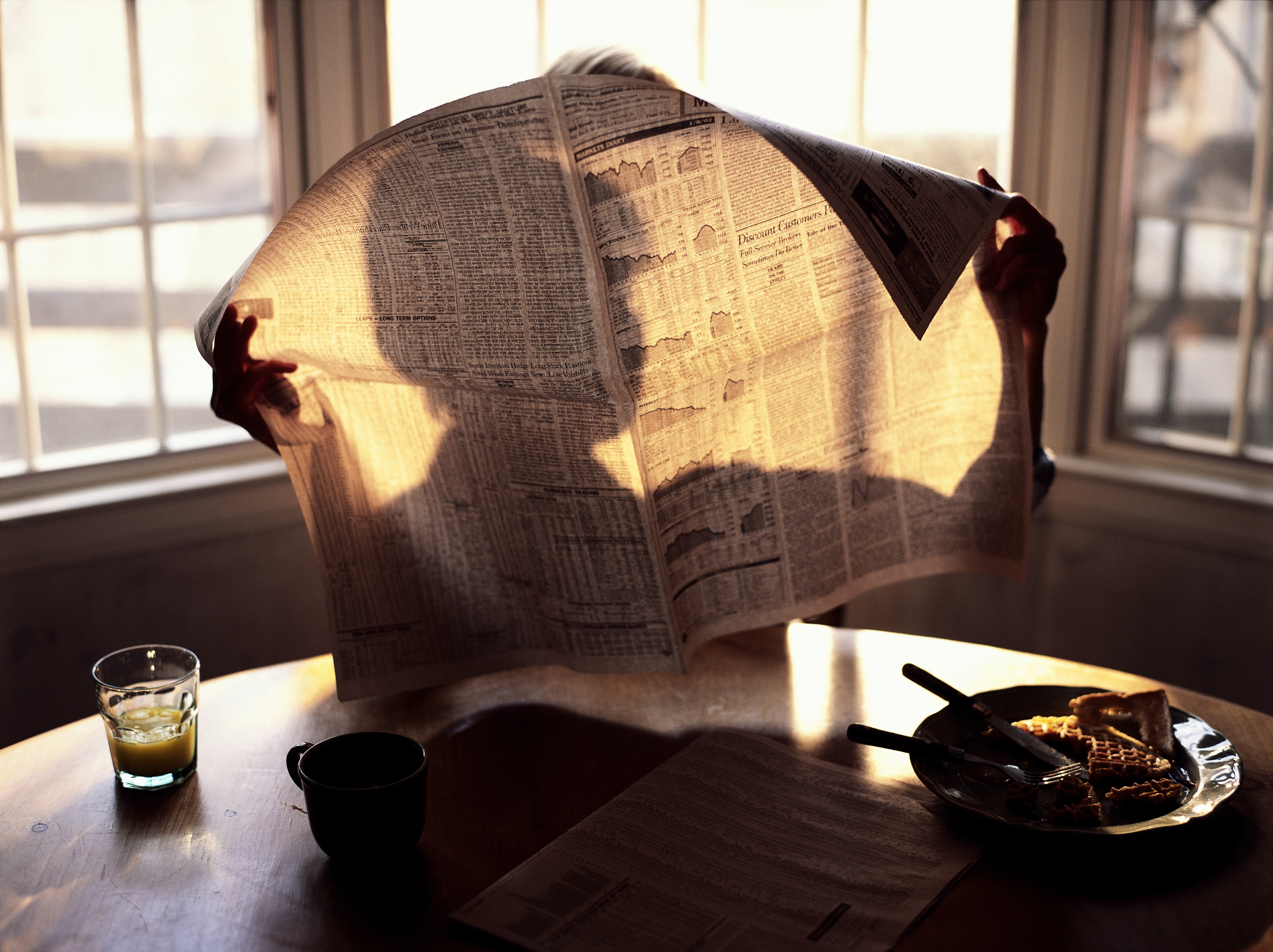 Silhouette of someone reading the newspaper, through the paper. Sunny